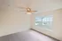 Primary bedroom with oversized window offering views of the community, neutral wall color, soft carpet flooring, and a ceiling fan for comfort.