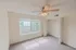 Spacious bedroom with plush carpeting, a large window with horizontal blinds, ceiling fan, and a double-door closet offering ample storage.