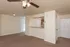 Living area at Embassy Ozark Apartments in Ozark, MO, featuring brown carpet, ceiling fan with lights, and an open breakfast bar overlooking the kitchen. White doors lead to additional rooms and storage.