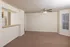Open living room at Embassy Ozark Apartments in Ozark, MO, with brown carpet, ceiling fan with lights, large window with blinds, and a breakfast bar view into the kitchen.