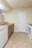 Embassy Ozark kitchen with tan tile flooring, double-basin sink, wood cabinetry, white dishwasher, electric stove, and a closed pantry door in a neutral-toned space.