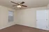 Bedroom at Embassy Ozark Apartments featuring brown carpet, a ceiling fan with lights, a single window with blinds, and a white door leading to the hallway. Walls are painted a soft beige with white trim.