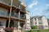 Three-story tan apartment building at Cobblestone Village 55+ community in Springfield, MO, featuring private balconies, wood railings, and a landscaped entry with accessible walkways.