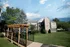 Charming wooden pergola covering a black-railed bridge leading through the grassy courtyard of Cobblestone Village, offering scenic, walkable access to amenities.