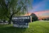 Monument sign for Cobblestone Village 55+ community on S. Ingram Mill Road in Springfield, MO, surrounded by green lawn and trees, with a sunset in the background.