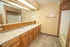 Bathroom with a long double sink vanity, wood cabinetry, oversized mirror, tiled walls, and bathtub.