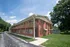 Angled exterior view of East Manor Apartments showing the two story red brick building, wooden balcony walkway, and surrounding lawn.