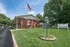 East Manor Apartments exterior with a red brick building, American flag, lawn, entrance sign, and mature trees.