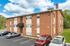 Charming brick apartment building with ample parking and lush greenery, under a bright blue sky.
