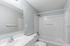 Bright and modern bathroom with sleek white fixtures, a spacious tub, and elegant mirror, offering a refreshing and tranquil atmosphere.