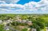 Scenic aerial view of a lush, green suburban neighborhood with modern brick apartment buildings and charming homes, under a vibrant blue sky with fluffy clouds.