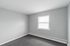 Bright and inviting room with soft gray walls, cozy carpeting, and a large window providing ample natural light.