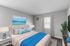 Inviting virtually staged bedroom featuring a plush bed with blue accents, modern decor, natural light, and a serene beach artwork.