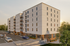 Modern apartment building with spacious balconies, large windows, and ample parking surrounded by lush greenery.