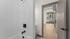 Modern apartment interior featuring a sleek white bathroom leading to a bright hallway with wooden floors and a cozy seating area by large windows.