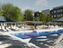 Luxurious apartment complex with a stunning outdoor pool, surrounded by modern lounge chairs and umbrellas, set against lush greenery and elegant architecture.