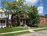 Charming brick townhouse nestled between leafy trees and vibrant greenery against a bright blue sky.