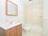 Tiled shower with white tub and brown vanity in apartment bathroom