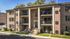 Front view of a charming brick apartment building with balconies and lush greenery.