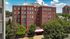 Charming red brick apartment building with lush greenery and a welcoming entrance under a clear blue sky.