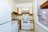 Charming galley kitchen with sleek white appliances, warm wood accents, and a large window offering natural light.