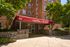 Charming brick apartment building entrance with a welcoming red awning at Gilpin Place, surrounded by lush greenery and elegant stonework.