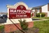 Inviting entrance sign for Mayflower Crossing Apartments surrounded by lush landscaping and modern brick buildings under a clear blue sky.