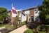 Charming brick apartment building with vibrant flower gardens and American flag, set against a clear blue sky.