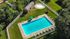 Aerial view of a luxurious apartment community with a sparkling swimming pool, surrounded by lush greenery and poolside lounge chairs.
