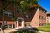 Charming brick apartment building with lush greenery and large windows, offering a welcoming entryway under a sunny blue sky.