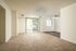 Bright and airy living room with modern carpeted flooring, large window, and sliding glass door leading to outdoor space.