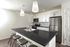 Modern kitchen with sleek black countertops, stylish white cabinetry, and stainless steel appliances; features an inviting island with pendant lighting and contemporary bar stools.