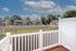 Peaceful apartment balcony view overlooking modern townhouses and spacious parking area, surrounded by lush greenery and blue skies.
