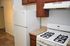 Modern kitchen with a sleek white gas stove, spacious fridge, and elegant wooden cabinetry, ideal for culinary enthusiasts.