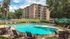 Sunny apartment complex with a sparkling pool, surrounded by lounge chairs and umbrellas, perfect for relaxation and leisure.