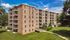 Charming brick apartment building with multiple balconies and beautifully landscaped surroundings on a sunny day.