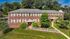 Charming brick apartment building with lush landscaping, scenic greenery, and inviting red doors, ideal for serene living.