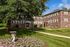 Charming brick apartment complex with lush green lawns, floral landscaping, and tree-lined paths.
