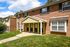 Charming brick apartment building with inviting entryway and manicured green lawn, basking under a clear blue sky.