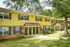Charming townhouse community with vibrant yellow and brick facade, surrounded by lush greenery and inviting pathways.