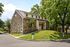 Charming stone-front house with lush green surroundings, featuring colonial architecture and a welcoming entrance.