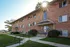 Charming brick apartment exterior with sunlit morning glow, lush green lawn, and welcoming entrance.