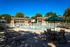 Charming residential complex featuring a sparkling outdoor pool with lounge chairs and shaded seating under sunny blue skies.
