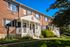 Charming brick apartment building with cozy white porches, surrounded by lush greenery and bright blue sky.