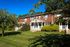 Charming brick townhouse with inviting porches surrounded by lush greenery under a clear blue sky.