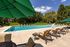 Inviting outdoor pool area with comfortable lounge chairs and shaded tables, nestled in a lush green setting offering a perfect relaxation spot.