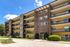 Charming multi-story apartment building with spacious balconies, surrounded by lush greenery and vibrant landscaping under a bright blue sky.