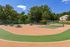 Vibrant outdoor recreation area featuring a tennis court, picnic tables, and a playground amidst lush greenery.
