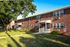 Charming brick apartment complex with lush green lawns, shaded by mature trees, and inviting porches for a welcoming ambiance.