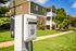 Charming apartment building with a modern EV charging station in a lush green setting.